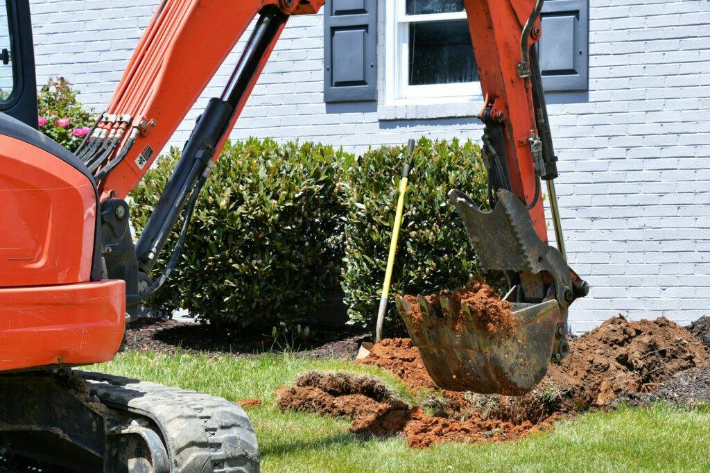 Backhoe digging dirt in lawn to install electrical & gas lines. Digging hole in yard. Scoopful soil